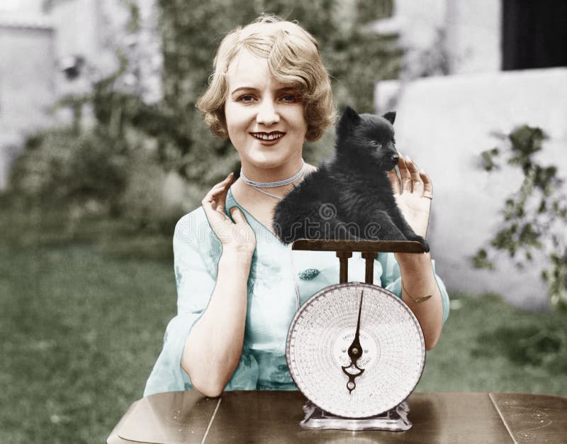 Portrait of a young woman weighing her puppy on a weighing scale