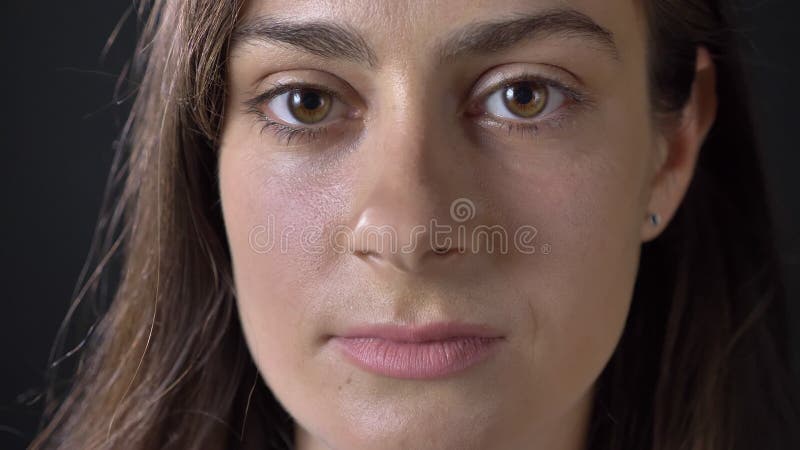 Portrait étroit de la jeune belle femme sérieuse regardant l'appareil-photo, d'isolement sur le fond noir clips vidéos
