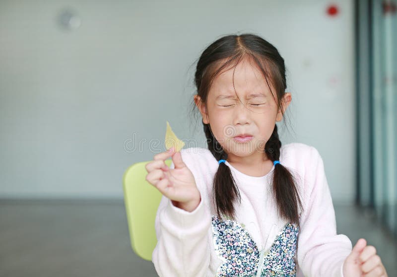 Portraits of cute Asian little girl eating crispy potato chips with face emotion feeling sour royalty free stock photo Portraits of cute Asian little girl eating crispy potato chips with face emotion feeling sour royalty free stock photo
