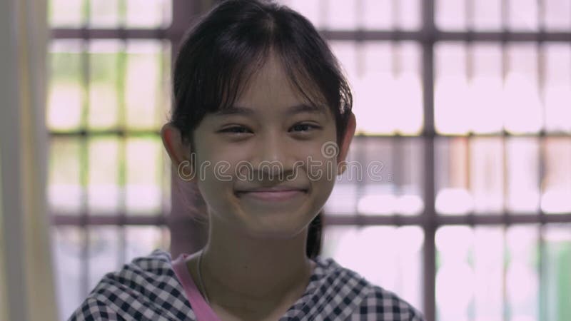 Portret azjatycki ładna nastolatka w przypadkowej sukience uśmiechnięta podczas oglądania kamery w salonie.