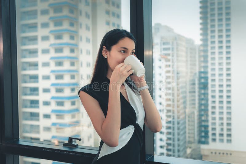 Portret bizneswoman Opowiada Someone na telefonie komórkowym i Pije filiżanka kawy Podczas gdy Stojący Przeciw okno fotografia royalty free Portret bizneswoman Opowiada Someone na telefonie komórkowym i Pije filiżanka kawy Podczas gdy Stojący Przeciw okno fotografia royalty free