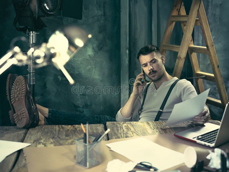 Portrait of a bearded businessman who is working with his notebook and mobile phone at loft studio or home. Portrait of a bearded businessman who is working with his notebook and mobile phone at loft studio or home.