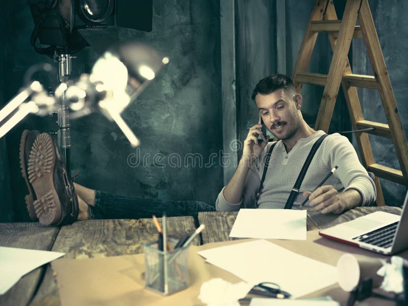 Portrait of a bearded businessman who is working with his notebook and mobile phone at loft studio or home. Portrait of a bearded businessman who is working with his notebook and mobile phone at loft studio or home.