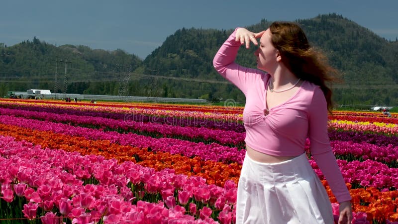Portret ciekawej młodej kobiety na polu tulipan trzymającej dłoń nad oczami i patrzącej w dal