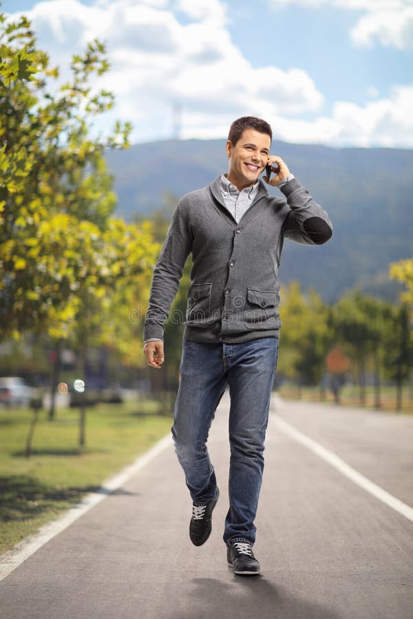 Portret de lungime completă a unui tip care merge și folosește un telefon stock photos