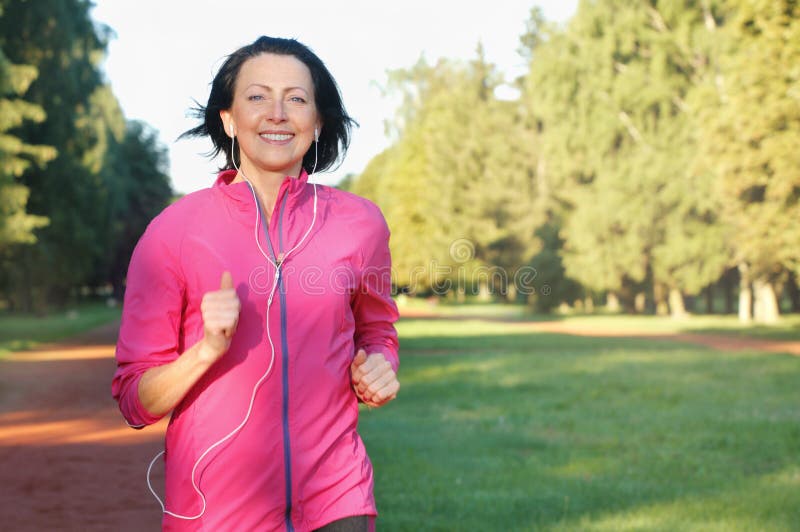 Portrait of elderly woman running with headphones in the park in early morning. Attractive looking mature woman keeping fit and healthy. Portrait of elderly woman running with headphones in the park in early morning. Attractive looking mature woman keeping fit and healthy.