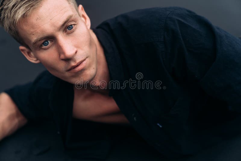 Portret die van de knappe blauw-eyed mens in zwart overhemd op zwart zandstrand liggen stock foto's Portret die van de knappe blauw-eyed mens in zwart overhemd op zwart zandstrand liggen stock foto's