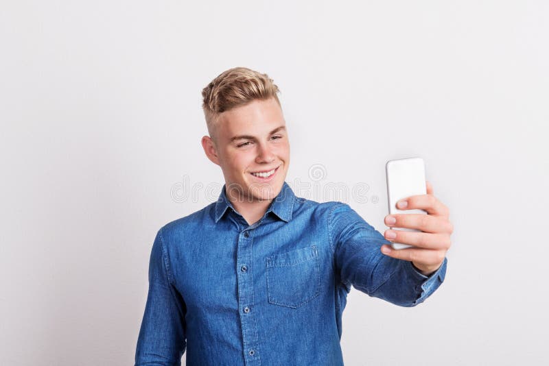 Portret die van een gelukkige jonge mens met een smartphone in een studio, selfie nemen stock foto's Portret die van een gelukkige jonge mens met een smartphone in een studio, selfie nemen stock foto's