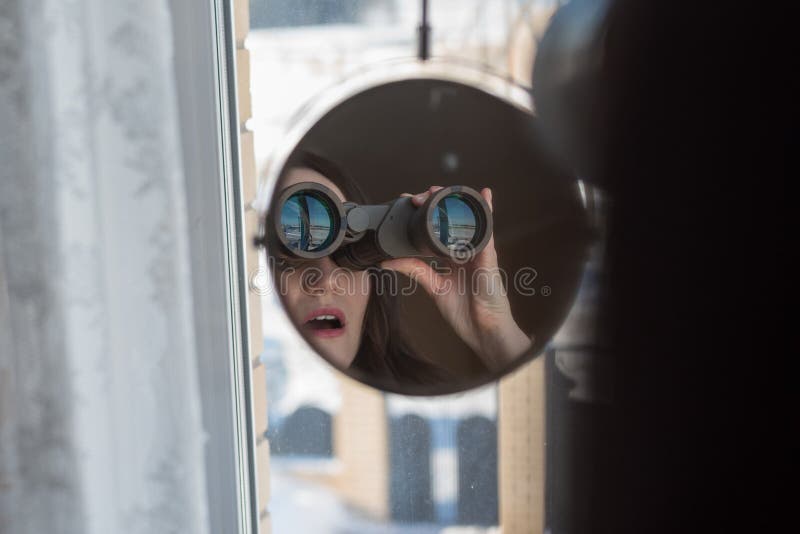 Portret die van een verrast brunette met verrekijkers die uit het venster, op buren spioneren kijken stock afbeelding Portret die van een verrast brunette met verrekijkers die uit het venster, op buren spioneren kijken stock afbeelding
