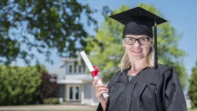 Portret die van een vrouw in een mantel en een graduatie GLB, een diploma in haar hand houden tegen de achtergrond van haar huis royalty-vrije stock fotografie Portret die van een vrouw in een mantel en een graduatie GLB, een diploma in haar hand houden tegen de achtergrond van haar huis royalty-vrije stock fotografie