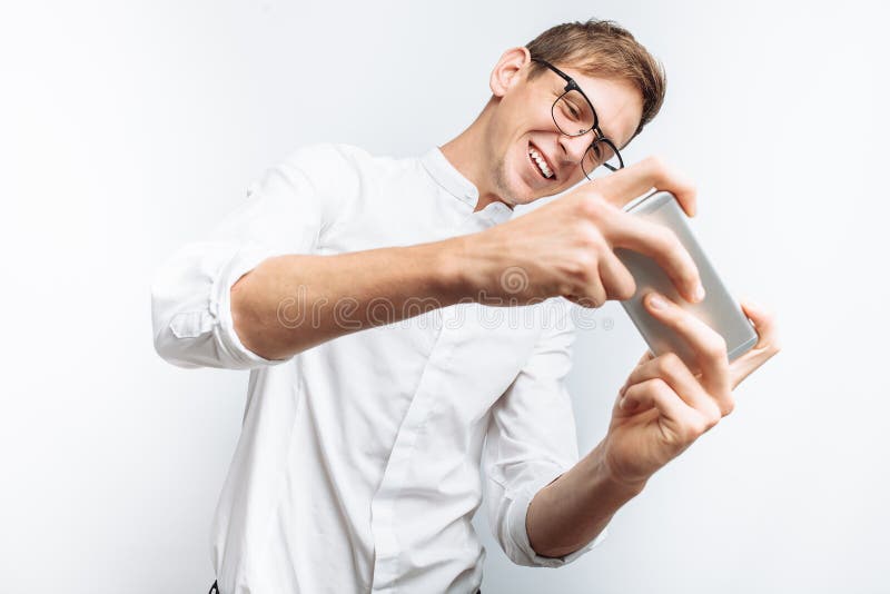 Portret die van jonge aantrekkelijke kerel in glazen spelen op telefoon, in wit die overhemd spelen op witte achtergrond, voor re stock afbeeldingen Portret die van jonge aantrekkelijke kerel in glazen spelen op telefoon, in wit die overhemd spelen op witte achtergrond, voor re stock afbeeldingen