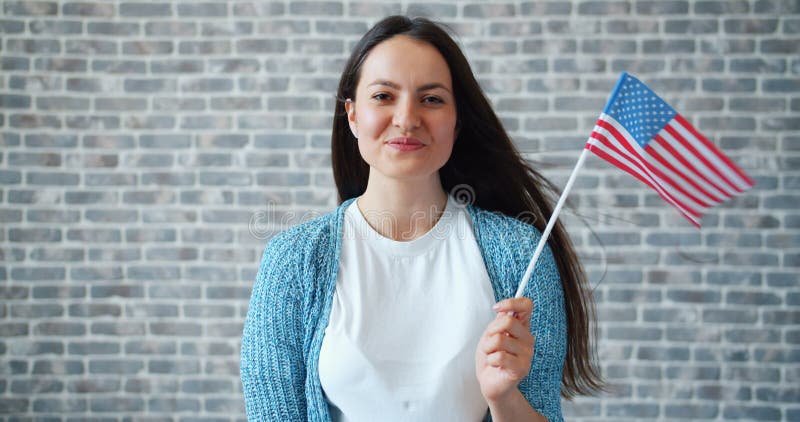 Portret die van leuk meisje Amerikaanse vlag houden en op bakstenen muurachtergrond glimlachen