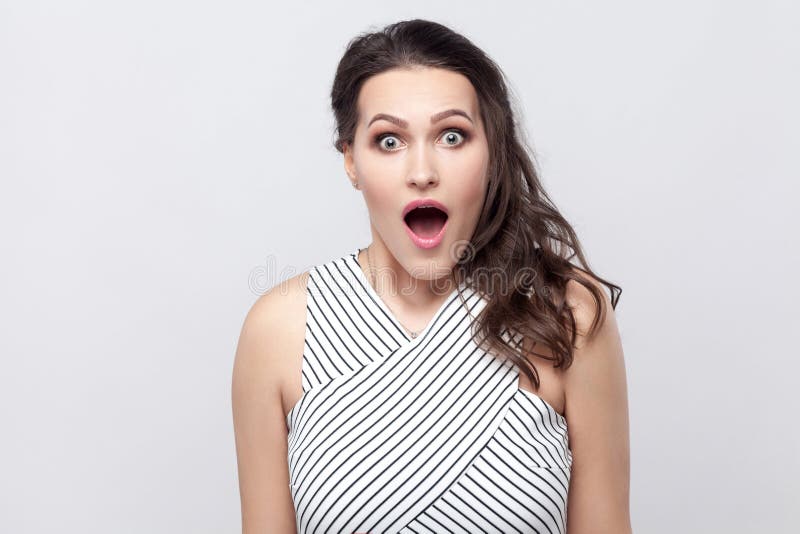 Portret die van verbaasde mooie jonge donkerbruine vrouw met make-up en gestreepte kleding die, camera met grote ogen het bekijke stock afbeeldingen Portret die van verbaasde mooie jonge donkerbruine vrouw met make-up en gestreepte kleding die, camera met grote ogen het bekijke stock afbeeldingen