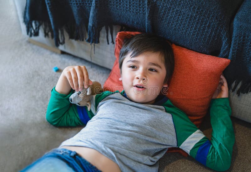 Portrait happy boy lying on carpet playing with dog toy while watching TV, Cute Child boy lying on floor relaxing and having fun on his own at home, Positive Children concept. Portrait happy boy lying on carpet playing with dog toy while watching TV, Cute Child boy lying on floor relaxing and having fun on his own at home, Positive Children concept