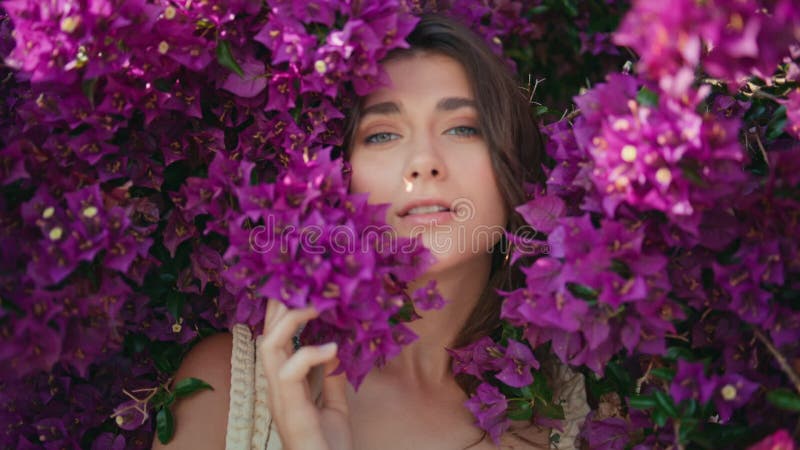 Portret glimlachende vrouw die camera ziet in violetbloemen bush. modelgezicht