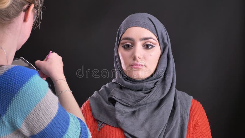 Portret makijażu artysta stawia na highlighter z płaskim muśnięciem na twarzy atrakcyjna muzułmańska kobieta w hijab w szkłach