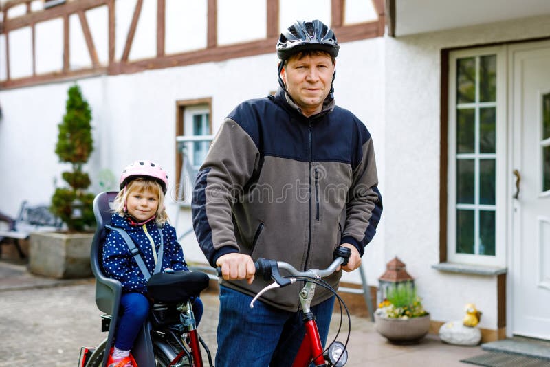 Portret małej dziewczynki z hełmem na głowie siedzącej na fotelu rowerowym i jej ojciec z rowerami. bezpieczny obraz stock