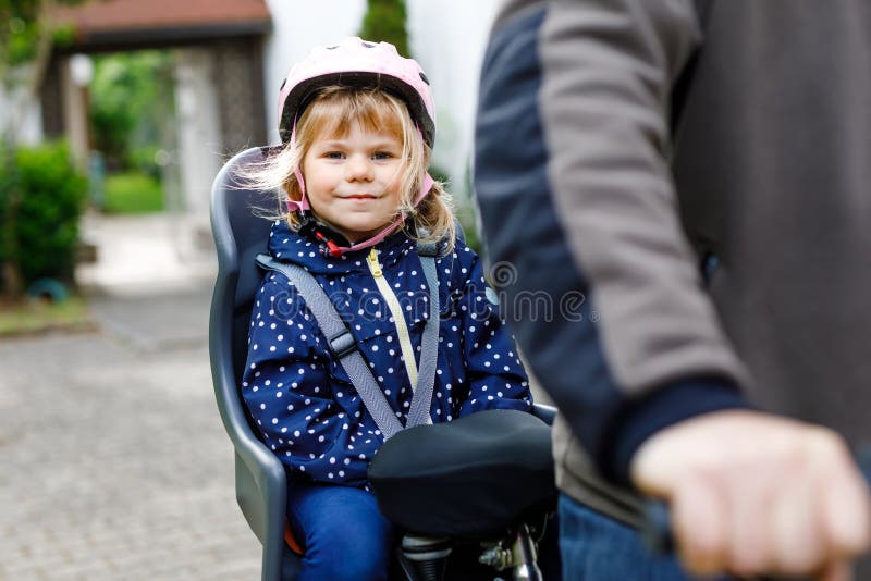 Portret małej dziewczynki z hełmem na głowie siedzącej na fotelu rowerowym i jej ojciec z rowerami. bezpieczny obraz royalty free