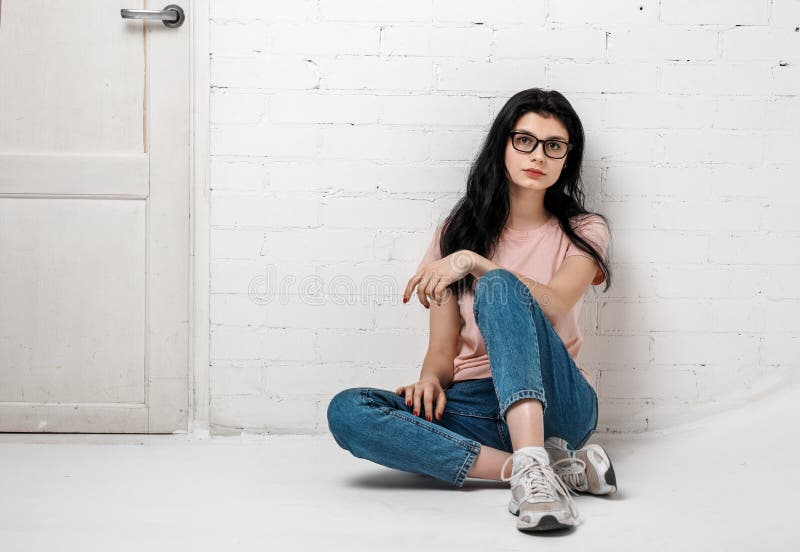 Portret mądrze piękna brunetki dziewczyna siedzi blisko białego ściana z cegieł w eyeglasses z naturalnym makijażem obrazy royalty free Portret mądrze piękna brunetki dziewczyna siedzi blisko białego ściana z cegieł w eyeglasses z naturalnym makijażem obrazy royalty free