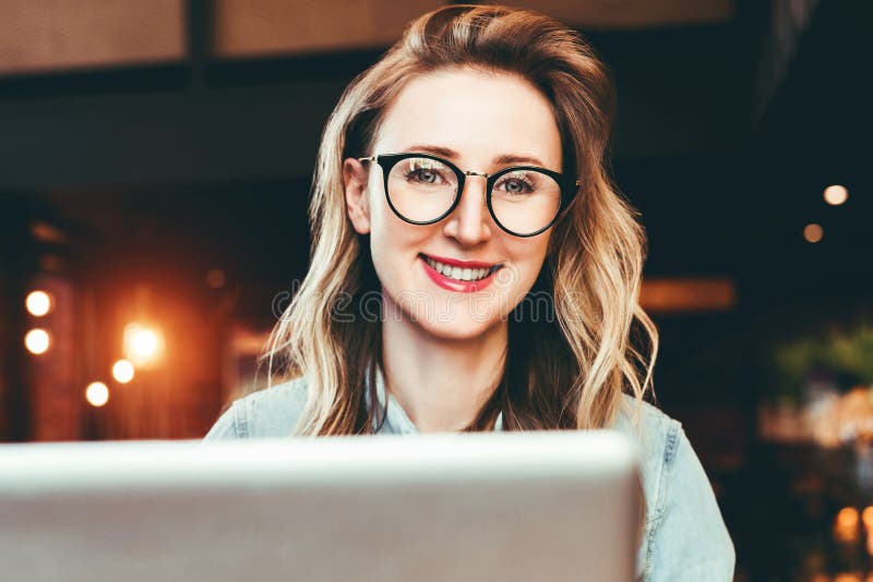 Portret młoda biznesowa kobieta siedzi w kawiarni w modnych szkłach, pracuje na laptopie Blogger komunikuje z zwolennikami fotografia stock Portret młoda biznesowa kobieta siedzi w kawiarni w modnych szkłach, pracuje na laptopie Blogger komunikuje z zwolennikami fotografia stock