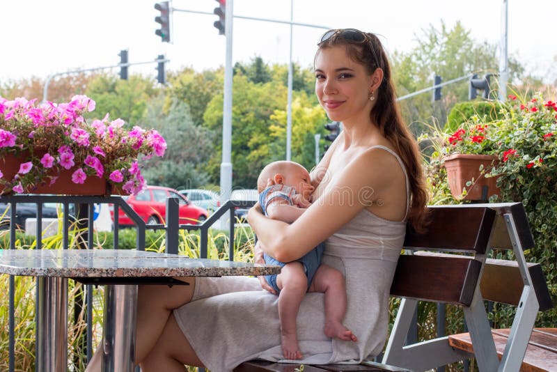 Portret młoda kobieta, szczęśliwa nowa matka pielęgnuje ślicznego dziecka obsiadanie na ławce dziecko, podczas gdy breastfeeding zdjęcie royalty free Portret młoda kobieta, szczęśliwa nowa matka pielęgnuje ślicznego dziecka obsiadanie na ławce dziecko, podczas gdy breastfeeding zdjęcie royalty free
