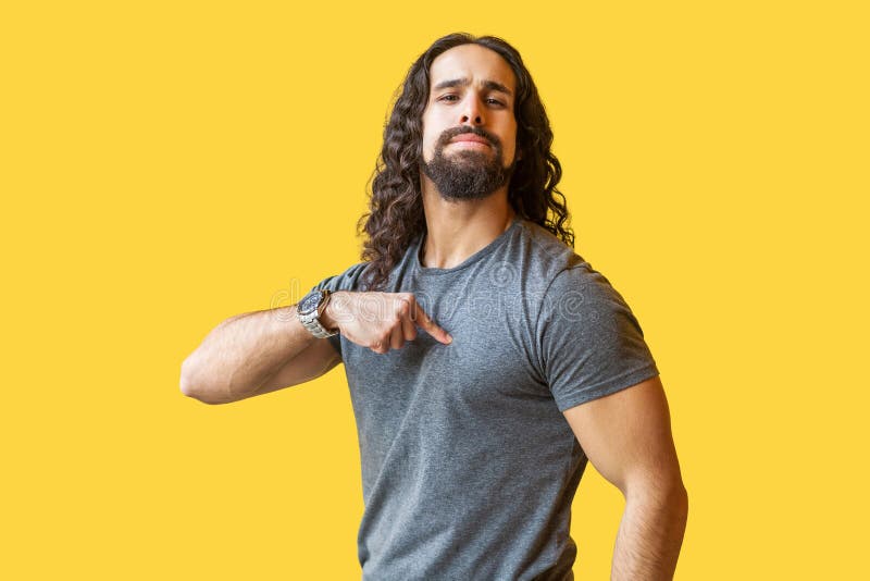 Portrait of proud bearded young man with long curly hair in grey tshirt standing, pointing himself and looking at camera with confident serious face. indoor studio shot isolated on yellow background. Portrait of proud bearded young man with long curly hair in grey tshirt standing, pointing himself and looking at camera with confident serious face. indoor studio shot isolated on yellow background