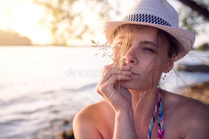 Portret piękna dziewczyna w kapeluszu z słomianym ostrzem trawa przeciw lata jeziornemu tłu przy zmierzchem na ciepłym wieczór zdjęcia stock Portret piękna dziewczyna w kapeluszu z słomianym ostrzem trawa przeciw lata jeziornemu tłu przy zmierzchem na ciepłym wieczór zdjęcia stock