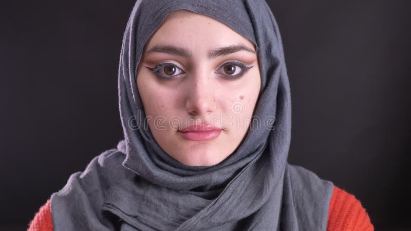 Portret piękna muzułmańska kobieta ogląda poważnie w kamerę na czarnym tle w hijab z jaskrawym makijażem