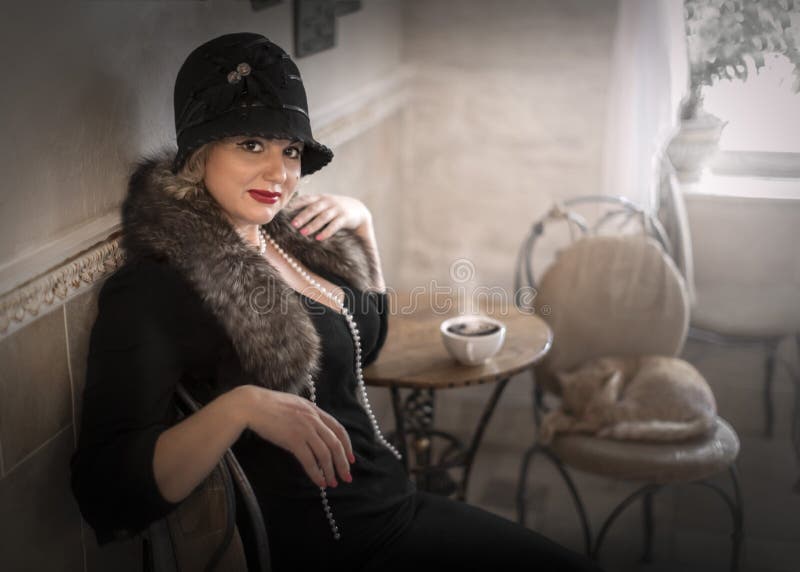 Portret pięknej kobiety w kapeluszu i futrzanym boa siedzącego przy stole z filiżanką kawy w kawie obraz stock