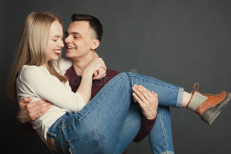 Portret piękni potomstwa dobiera się w miłości pozuje przy studiiem nad ciemnym tłem Facet trzyma jego ukochanego w jego smil i r zdjęcie royalty free Portret piękni potomstwa dobiera się w miłości pozuje przy studiiem nad ciemnym tłem Facet trzyma jego ukochanego w jego smil i r zdjęcie royalty free