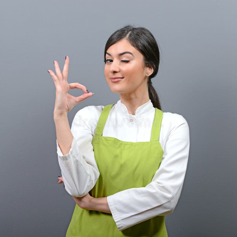 Portret piękny kobieta szef kuchni pokazuje ok znaka przeciw szaremu tłu zdjęcia stock Portret piękny kobieta szef kuchni pokazuje ok znaka przeciw szaremu tłu zdjęcia stock