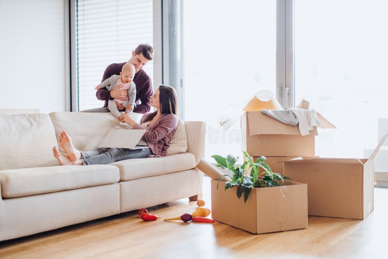 A portrait of happy young couple with a baby,laptop and cardboard boxes, moving in a new home. A portrait of happy young couple with a baby,laptop and cardboard boxes, moving in a new home.