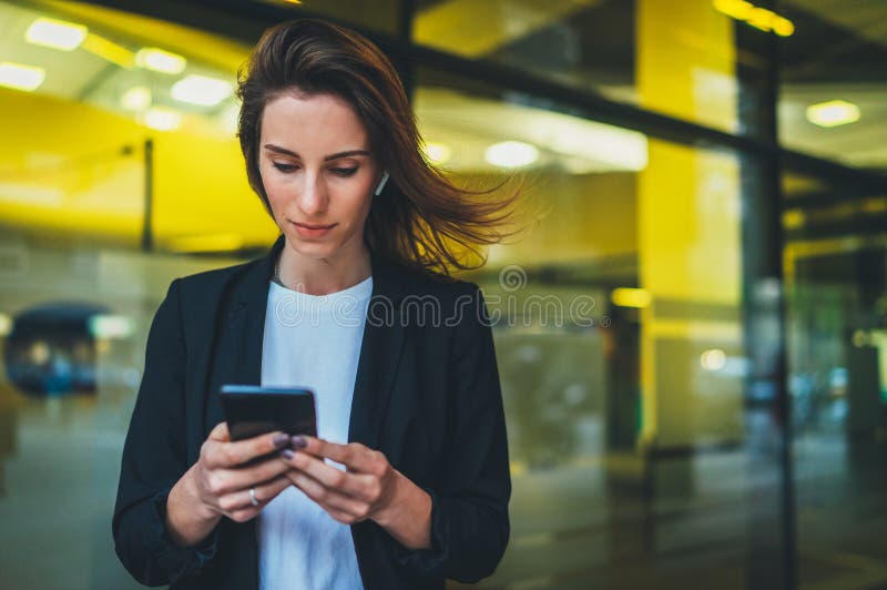 Portrait professional female finance lawyer standing near office in evening street communicates online by cellphone. successful businesswoman pushing message to colleagues on mobile phone on background yellow neon lights. Portrait professional female finance lawyer standing near office in evening street communicates online by cellphone. successful businesswoman pushing message to colleagues on mobile phone on background yellow neon lights