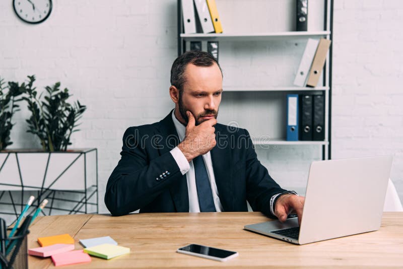 Portret skupiający się biznesmen pracuje na laptopie przy miejscem pracy zdjęcie stock Portret skupiający się biznesmen pracuje na laptopie przy miejscem pracy zdjęcie stock