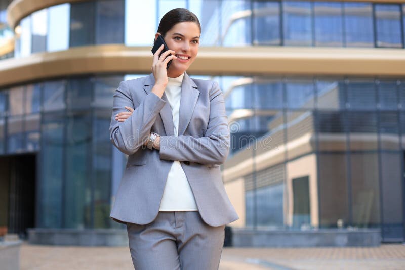 Portret stylowej, uśmiechniętej kobiety biznesowej w modnych ubraniach, dzwoniącej na telefon komórkowy w pobliżu biura obraz stock Portret stylowej, uśmiechniętej kobiety biznesowej w modnych ubraniach, dzwoniącej na telefon komórkowy w pobliżu biura obraz stock