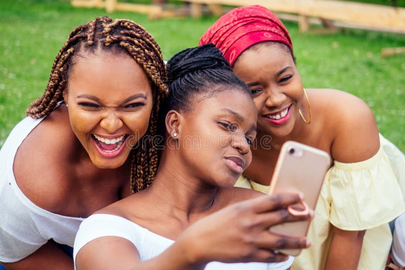 Portrait of three beautiful african-american women afro braids dreadlocks and turban taking pictures of yourself on the phone in the park at a picnic,sisters on vacation. Portrait of three beautiful african-american women afro braids dreadlocks and turban taking pictures of yourself on the phone in the park at a picnic,sisters on vacation.