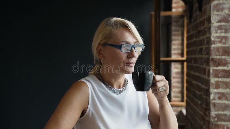 Portret urocza? rodkowa rok kobieta w szk? ach pije kawowy siedz? cy pobliski nadokienny patrze? outside z szcz?? liwym zbiory wideo