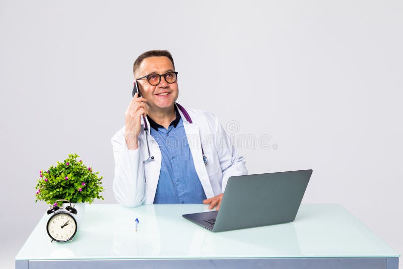 Portret uśmiechniętego lekarza przy użyciu laptopa i telefonu w gabinecie lekarskim fotografia stock