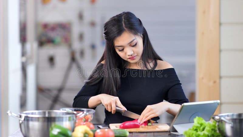 Portret van aanbiddelijke jonge Aziatische vrouwelijke huisvrouw tijdens kokende verse gezonde maaltijd bij keuken