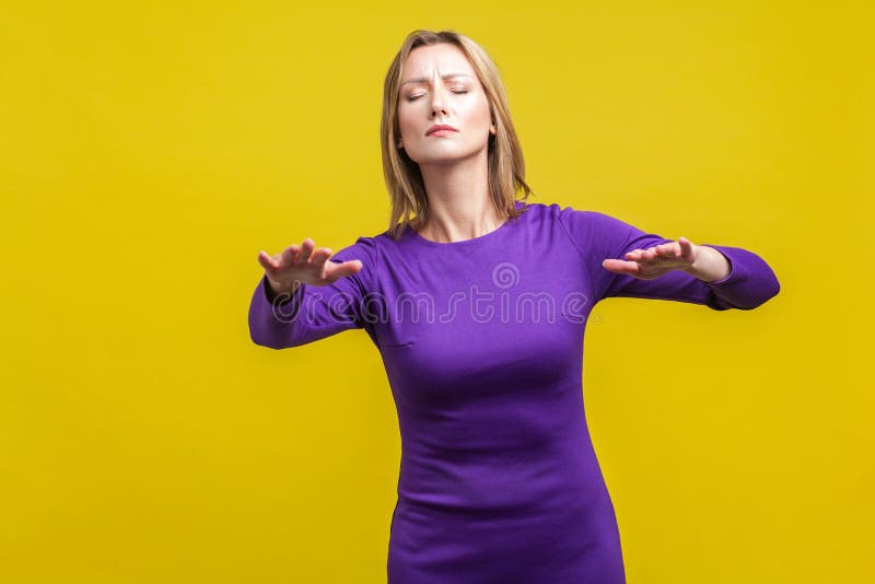 Portrait of blind disoriented young woman in elegant tight purple dress walking with closed eyes, reaching out hands to find lost way, vision loss. indoor studio shot isolated on yellow background. Portrait of blind disoriented young woman in elegant tight purple dress walking with closed eyes, reaching out hands to find lost way, vision loss. indoor studio shot isolated on yellow background