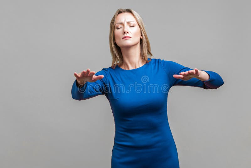 Portrait of blind disoriented young woman in elegant tight blue dress walking with closed eyes, reaching out hands to find lost way, vision loss. indoor studio shot isolated on gray background. Portrait of blind disoriented young woman in elegant tight blue dress walking with closed eyes, reaching out hands to find lost way, vision loss. indoor studio shot isolated on gray background