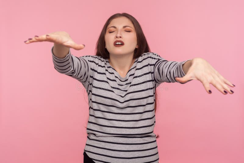 Portrait of blind disoriented woman in striped sweatshirt walking with closed eyes, trying to touch, find obstacles in darkness, vision problems. indoor studio shot isolated on pink background. Portrait of blind disoriented woman in striped sweatshirt walking with closed eyes, trying to touch, find obstacles in darkness, vision problems. indoor studio shot isolated on pink background