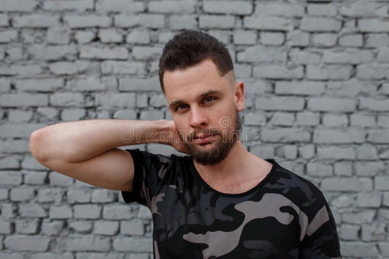 Portret van de aantrekkelijke jonge knappe mens met een modieus kapsel en brutale baard in een modieuze camouflage militaire t-sh royalty-vrije stock foto's Portret van de aantrekkelijke jonge knappe mens met een modieus kapsel en brutale baard in een modieuze camouflage militaire t-sh royalty-vrije stock foto's