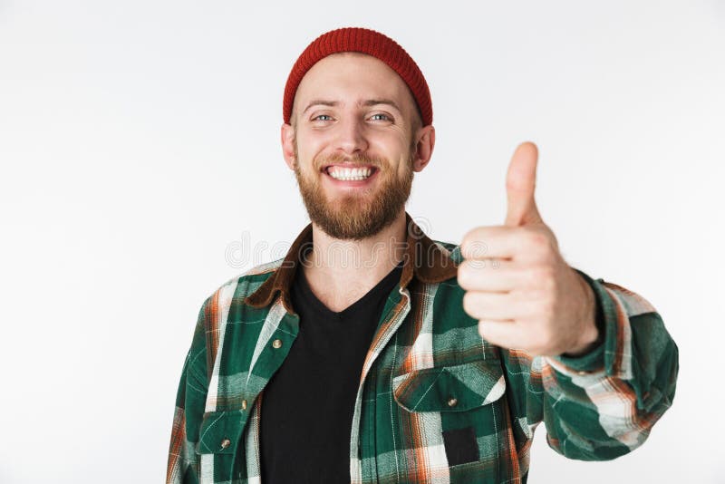 Portret van de Europese gebaarde mens die hoed en plaidoverhemd dragen die duim tonen, terwijl status geïsoleerd over witte achte royalty-vrije stock foto Portret van de Europese gebaarde mens die hoed en plaidoverhemd dragen die duim tonen, terwijl status geïsoleerd over witte achte royalty-vrije stock foto