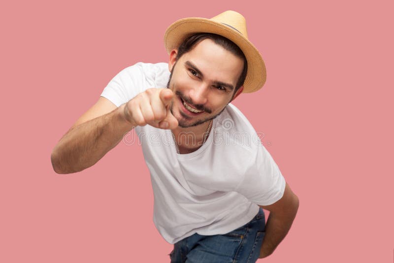 Portret van de grappige gebaarde jonge mens in wit overhemd met hoed die, en camera met toothy glimlach richten bekijken bevinden stock afbeeldingen Portret van de grappige gebaarde jonge mens in wit overhemd met hoed die, en camera met toothy glimlach richten bekijken bevinden stock afbeeldingen