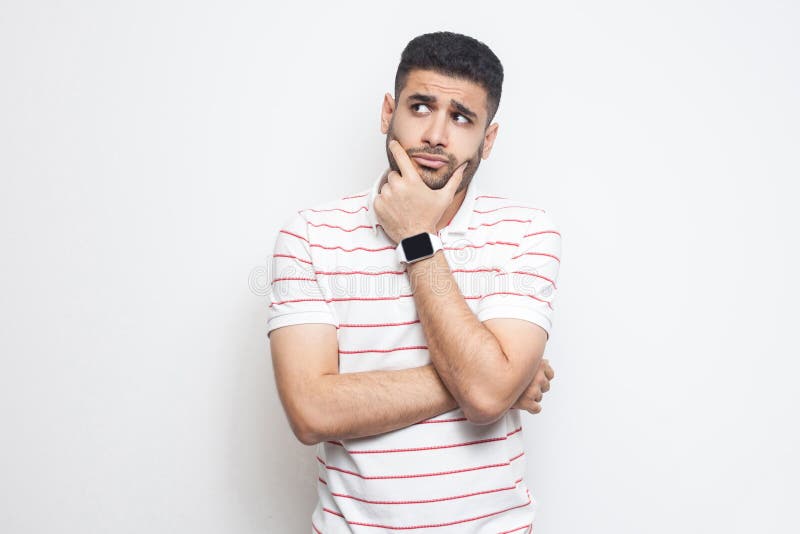 Portret van de peinzende knappe gebaarde jonge mens in gestreepte t-shirt die, zich wat betreft zijn gezicht bevinden, opzij weg stock foto Portret van de peinzende knappe gebaarde jonge mens in gestreepte t-shirt die, zich wat betreft zijn gezicht bevinden, opzij weg stock foto