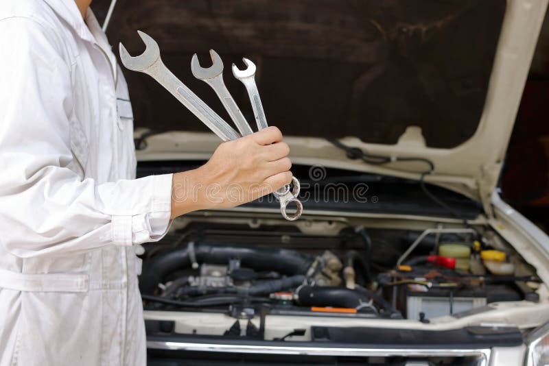Portret van de professionele jonge mechanische mens in witte eenvormige holdingsmoersleutels tegen auto in open kap bij de repara royalty-vrije stock afbeeldingen Portret van de professionele jonge mechanische mens in witte eenvormige holdingsmoersleutels tegen auto in open kap bij de repara royalty-vrije stock afbeeldingen
