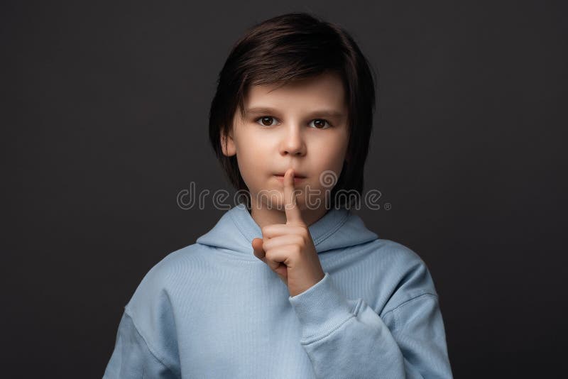 Portrait of Cute boy 10-12 years old, dressed in casual clothes holding index finger on lips. Silence and secret concept. Studio shot, gray background. Human emotions, facial expression concept. Portrait of Cute boy 10-12 years old, dressed in casual clothes holding index finger on lips. Silence and secret concept. Studio shot, gray background. Human emotions, facial expression concept