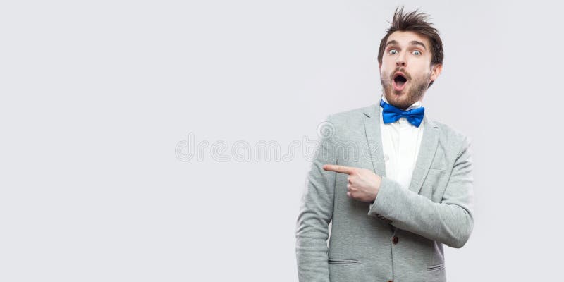 Portret van de verbaasde knappe gebaarde mens in toevallig grijs kostuum en blauwe vlinderdas status die camera met verrast gezic royalty-vrije stock afbeeldingen Portret van de verbaasde knappe gebaarde mens in toevallig grijs kostuum en blauwe vlinderdas status die camera met verrast gezic royalty-vrije stock afbeeldingen