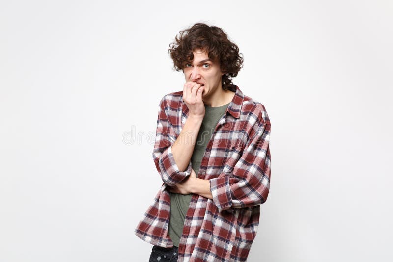 Portret van de zenuwachtige ontevreden jonge mens die in vrijetijdskleding camera, knagende die spijkers kijken op witte muur wor royalty-vrije stock foto's Portret van de zenuwachtige ontevreden jonge mens die in vrijetijdskleding camera, knagende die spijkers kijken op witte muur wor royalty-vrije stock foto's